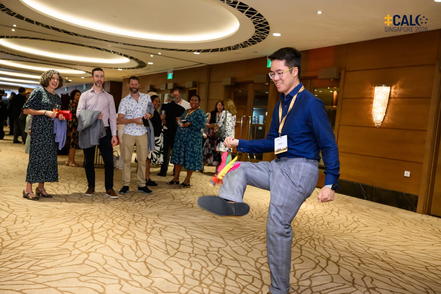 A delegate plays with a feathered shuttlecock during the Conference networking reception at The Fullerton Hotel Singapore, to the amusement of other delegates watching nearby.